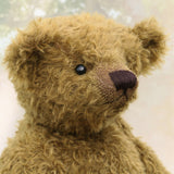 Close-up of a brownish-green teddy bear with a blurred light background