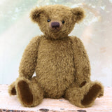 brownish-green teddy bear sitting on a wooden surface with a soft, blurred background