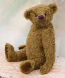 brownish-green teddy bear sitting on a wooden surface with a light background