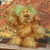 Green Eared Banana Stalker is a little, endearingly sweet and joyful, one of a kind, artist bear by Barbara-Ann Bears in wonderfully fluffy mohair, he stands 6.5 inches/17 cm tall. He is mostly made from a long golden mohair with brown tipping, with hand dyed green mohair ears, and beige wool felt paw pads. He has hand painted glass eyes with hand coloured eyelids, a wonderfully embroidered nose and a broad and cheerful smile.
