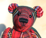 Red plaid teddy bear with black boot button eyes and a black nose on a beige background