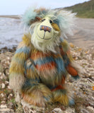 Colourful teddy bear on a rocky outcrop with ocean and beach  in the background