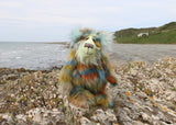 Colourful teddy bear on a rocky outcrop with ocean and beach  in the background