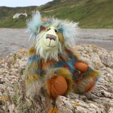 Colourful teddy bear sitting on a rocky outcrop with ocean and beach  in the background