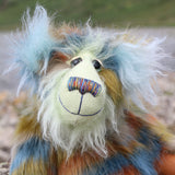 Close up of a colourful teddy bear with a textured fur pattern against a blurred natural background