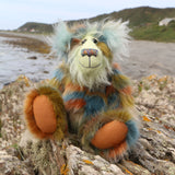 Colourful teddy bear sitting on a rocky outcrop with ocean and beach  in the background