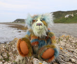 Colourful teddy bear sitting on a rocky outcrop with ocean and beach  in the background