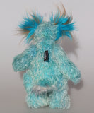 Billy Calypso is made from a sparse mohair hand dyed sky blue, his tummy is a long blue, yellow and magenta faux fur with black spots and his face and the underside of his tail are a long white mohair with blue tipping. On top of Billy's head and on the backs of his ears is a long aqua faux fur with tufts of warm beige. Billy has hand-dyed velvet paw pads. Billy has beautiful hand painted eyes with eyelids, a nose embroidered from individual threads and he has a huge, friendly smile