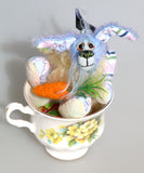 Bluebell is a small and sweet, one of a kind rabbit in beautifully coloured mohair and designer bunny fabric by Barbara Ann Bears, she stands just 5 inches/13 cm tall.  Bluebell is mostly made from a beautiful 'Peter Rabbit' cotton fabric with hand dyed blue and pale yellow mohair and hand dyed velvet paws, sitting in her Gainsborough cup with her carrot and Easter eggs