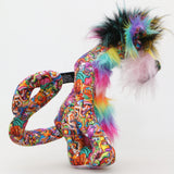 Faustus is mostly made from a very bright and colourful, monstrous cotton fabric. The sides of Faustus' face are a very long pale pink mohair with a dusky lavender-pink backcloth and the top of his nose is a long, fluffy mohair hand dyed yellow. His tummy and the backs of his ears are a long faux fur in bands like a rainbow and on top of his head he has a long black faux fur with plumes of yellow, magenta and teal. Faustus' footpads are made from hand dyed velvet.