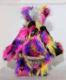 Miguel is mostly made from a very long, shaggy and dense faux fur which is black with bands of magenta, yellow, violet, grey and white. Miguel 's face, the fronts of his ears and the underside of his tail are made from a very long and soft white mohair. Miguel has large, beautiful, hand painted glass eyes with hand coloured eyelids, he has a carefully embroidered nose that incorporates all of his colours and a sweet, thoughtful smile
