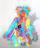 Pedro Piccolo is mostly made from a fairly long and fluffy multi-coloured faux fur in sky blue with flashes of yellow, magenta, orange and mauve. His face, the fronts of his ears and the underside of his tail are a very long and fluffy white mohair.  Pedro Piccolo has blue velvet paw pads which complement his colouring perfectly. He has beautiful, hand painted glass eyes with eyelids, a wonderful nose embroidered from individual threads to match his colouring and a charming smile