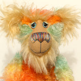 Close-up of Bossa Nova's face showing his long golden fur, his beautiful hand painted eyes, his multicoloured nose and broad smile. Bossa Nova is a 21 inch colourful, one of a kind, artist teddy bear in gorgeous hand dyed mohair by Barbara-Ann Bears