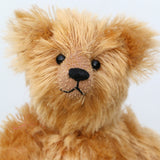 Close-up of Bruce Fettlewell is a cuddly little traditional one of a kind artist bear in antique gold German mohair with a soft texture on a light background