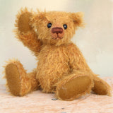 Bunbeary sitting and waving. Bunbeary is a well proportioned yet slightly raggedy traditional teddy bear. Bunbeary is made from beautiful distressed antique gold German mohair which has a warm tan backing, with wool felt paw pads, boot button eyes and a sweet smile.