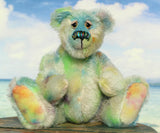 Colin Cockles a colourful hand dyed mohair teddy bear sitting on a wooden surface with a blue sky and clouds in the background