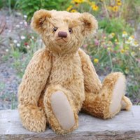 Teddy bear sitting on a wooden bench with a natural background of flowers and plants