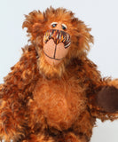 A close-up of Denzel, a happy brown tipped ginger mohair artist bear by Barbara A Bears, photographed standing against a plain light grey background.