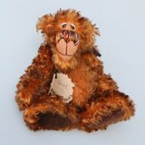 Denzel, a happy brown tipped ginger mohair artist bear by Barbara A Bears, photographed sitting against a plain light grey background.This photo shows his original swing ticket.