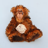 Denzel, a happy brown tipped ginger mohair artist bear by Barbara A Bears, photographed sitting against a plain light grey background.This photo shows his original swing ticket.