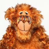 A close-up of Denzel's face, a happy brown tipped ginger mohair artist bear by Barbara A Bears, photographed sitting against a plain light grey background.