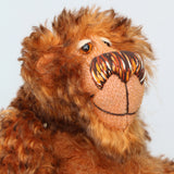A close-up of Denzel's face, a happy brown tipped ginger mohair artist bear by Barbara A Bears, photographed sitting against a plain light grey background.