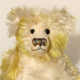 The face of Dorothy teddy bear, a yellow and white hand dyed mohair teddy bear with a multicoloured nose and black glass eyes against a white background