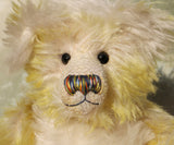 The face of Dorothy teddy bear, a yellow and white hand dyed mohair teddy bear with a multicoloured nose and black glass eyes against a white background