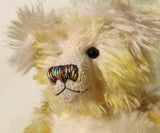 The face of Dorothy teddy bear, a yellow and white hand dyed mohair teddy bear with a multicoloured nose and black glass eyes against a white background