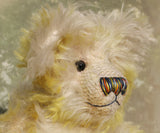 The face of Dorothy teddy bear, a yellow and white hand dyed mohair teddy bear with a multicoloured nose and black glass eyes against a white background