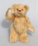 Euan, a mohair collector's teddy bear with a soft texture  waving on a light grey background