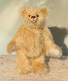 Euan, a mohair collector's teddy bear with a soft texture standing on a wooden surface with a light background