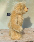 Euan in profile, a mohair collector's teddy bear with a soft texture standing on a wooden surface with a neutral background