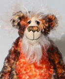 A close up of Flambé by Barbara Ann Bears, a handmade, distressed teddy bear with a long fluffy mohair face, with hand painted eyes, a multi coloured nose and a beaming smile. Made from shaggy brown and orange fur, a cream-coloured stitched face
