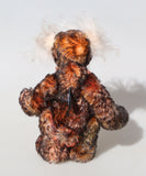 Back view of Flambé by Barbara Ann Bears, a handmade, distressed teddy bear with shaggy brown and orange fur, a cream-coloured stitched face, and colourful striped paw pads