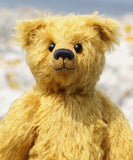 Close-up of Fortescue, a golden teddy bear by Barbara Ann Bears with shaggy fur sits on a rocky, grassy shoreline near Lochranza on the Isle of Arran, Scotland.