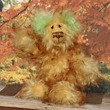 Green Eared Banana Stalker is a little, endearingly sweet and joyful, one of a kind, artist bear by Barbara-Ann Bears in wonderfully fluffy mohair, he stands 6.5 inches/17 cm tall. He is mostly made from a long golden mohair with brown tipping, with hand dyed green mohair ears, and beige wool felt paw pads. He has hand painted glass eyes with hand coloured eyelids, a wonderfully embroidered nose and a broad and cheerful smile. 