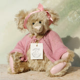 Little Rowena a vintage Barbara Ann teddy bear in a pink knitted cardigan with her name tag on a wooden surface
