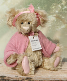 Little Rowena a vintage Barbara Ann teddy bear in a pink knitted cardigan with her name tag on a wooden surface