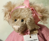 Close up of Little Rowena, a vintage Barbara Ann teddy bear in a pink knitted cardigan and pink ribbon