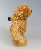 Side profile of Owen, a traditional antique gold teddy bear on a light grey background