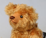 close up of Owen, a traditional antique gold teddy bear on a light grey background