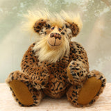 Tarzan McKenzie sitting. He is a very fashionable and exotic, one of a kind, artist bear by Barbara-Ann Bears in leopard print faux fur and fluffy gold mohair. He has ochre felt paw pads, hand painted glass eyes, a beautifully embroidered nose and a huge smile.