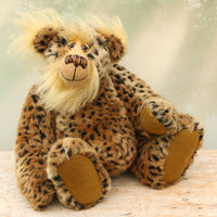 Tarzan McKenzie sitting. He is a very fashionable and exotic, one of a kind, artist bear by Barbara-Ann Bears in leopard print faux fur and fluffy gold mohair. He has ochre felt paw pads, hand painted glass eyes, a beautifully embroidered nose and a huge smile.