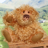 Plush teddy bear sitting on a wooden surface with a scenic background of mountains and greenery.