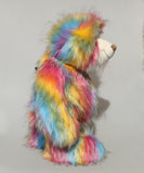 Cock A Doodle Doo in profile, a colourful, furry teddy bear with a shaggy, multi-hued coat in pink, yellow, blue, orange, and green, standing against a plain light grey background.