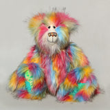 Cock A Doodle Doo, a colourful, furry teddy bear with a shaggy, multi-hued coat in pink, yellow, blue, orange, and green, sitting against a plain light grey background.