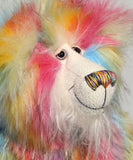 A close-up of Cock A Doodle Doo's face, a fluffy teddy bear with a rainbow fur pattern, featuring a white mohair face with hand painted glass eyes, a multicoloured nose and a sweet smile set against a plain light grey background.  