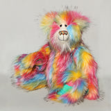 Cock A Doodle Doo, a colourful, furry teddy bear with a shaggy, multi-hued coat in pink, yellow, blue, orange, and green, sitting against a plain light grey background.