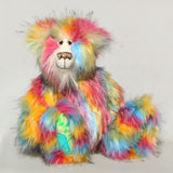 Cock A Doodle Doo, a colourful, furry teddy bear with a shaggy, multi-hued coat in pink, yellow, blue, orange, and green, sitting against a plain light grey background.
